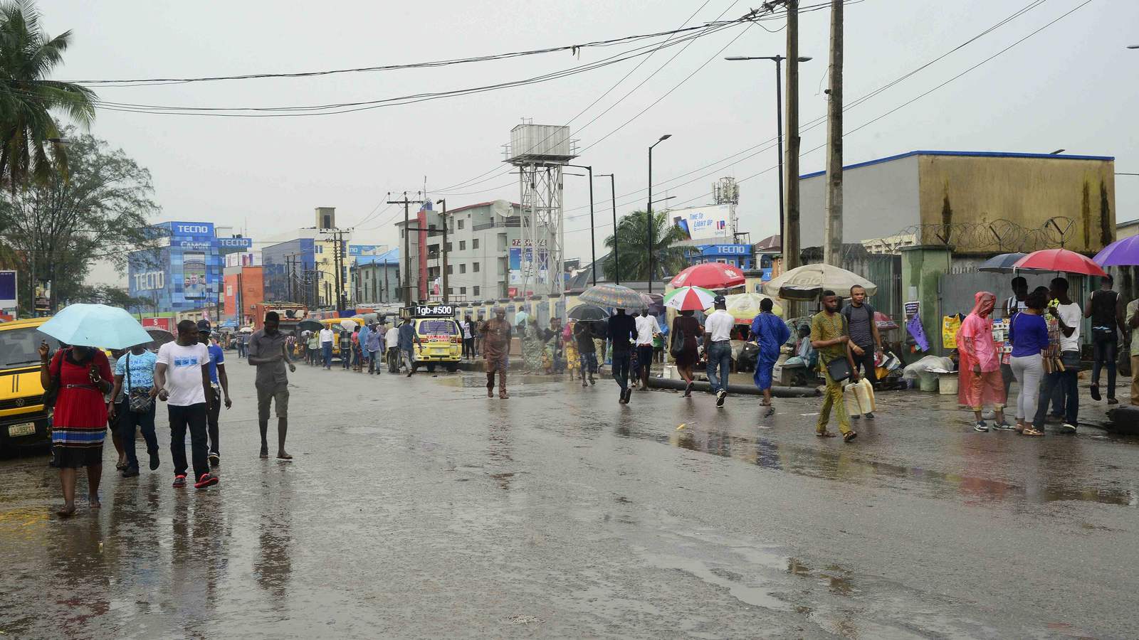 Shoppers with umbrellas on a rainy Lagos electronics market street in Ikeja