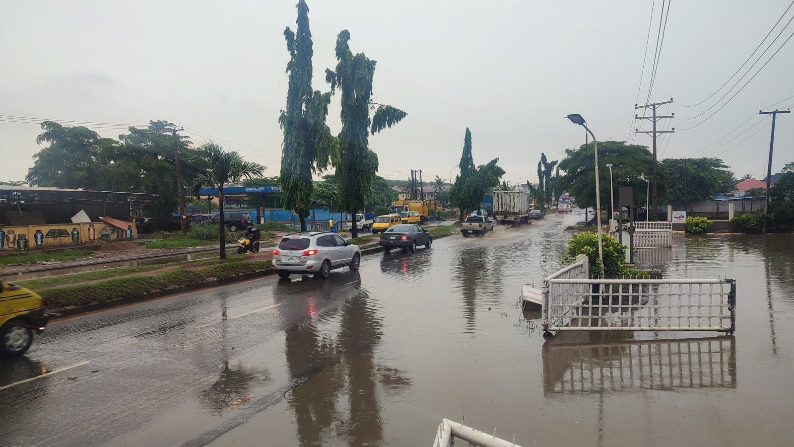 Flooded Lagos road with cars driving through standing water past a submerged gate