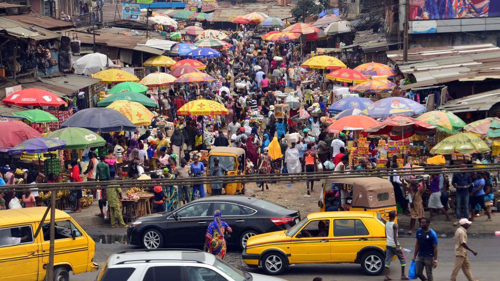 Crowded Lagos market street with trader umbrellas and yellow commercial buses