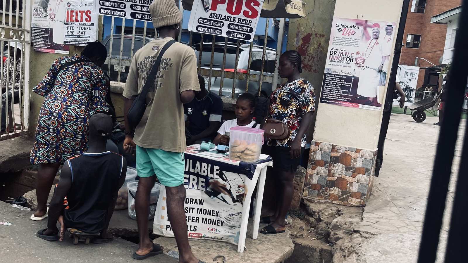Customers at a Nigerian street POS kiosk advertising cash withdrawal and money transfer