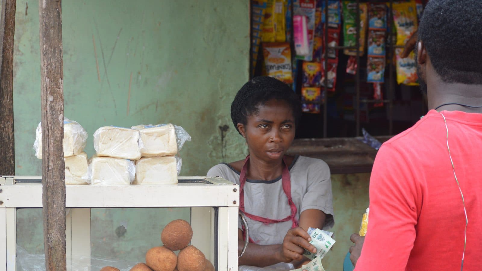 A Nigerian shopkeeper handing change to a customer across the counter of her provision store